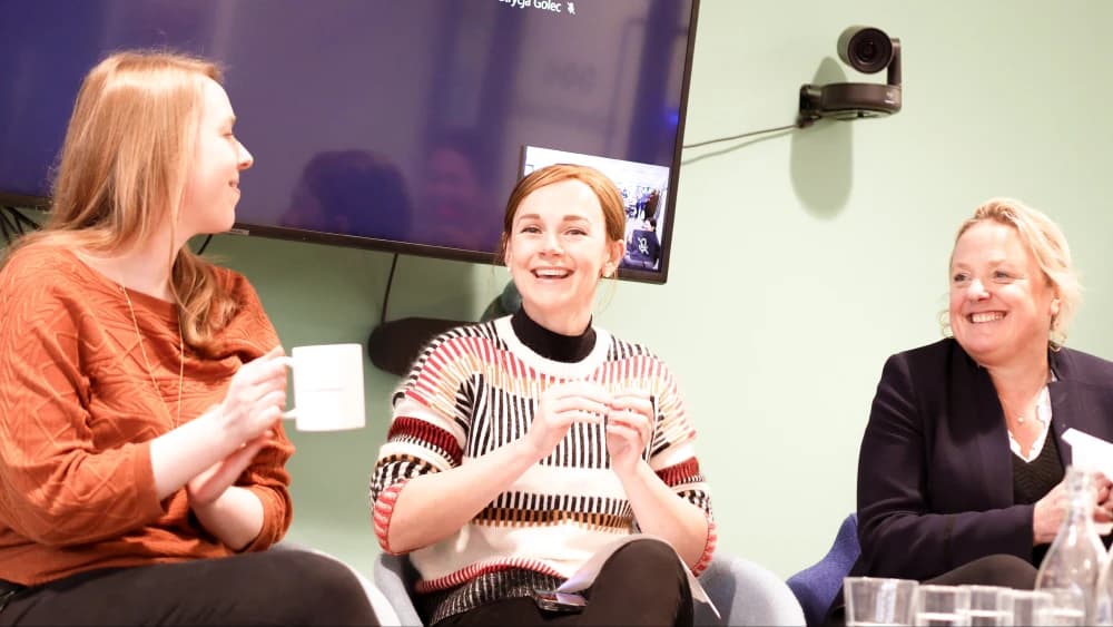 Teri (Director of Engineering), Lauren (CMO) and Katy (CEO) are sat together. They appear to be in front of an audience, hosting a conference. They are laughing.